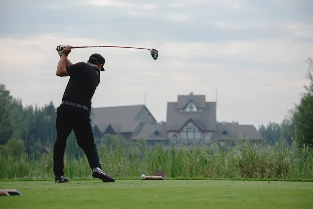 A man in golf attire swings a golf club on the tee