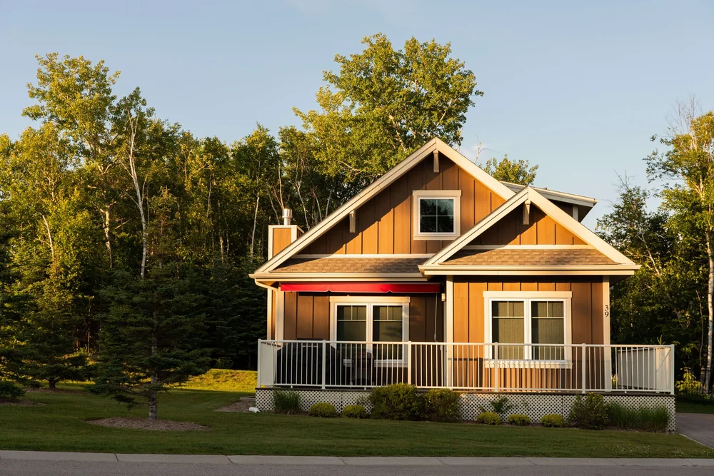 A two-storey cottage with brown siding, a covered porch and white trim