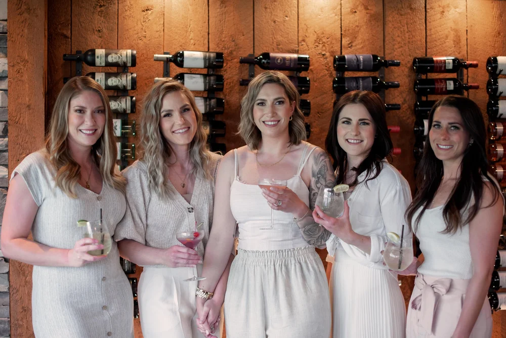 Three guests with drinks in front of a wine wall