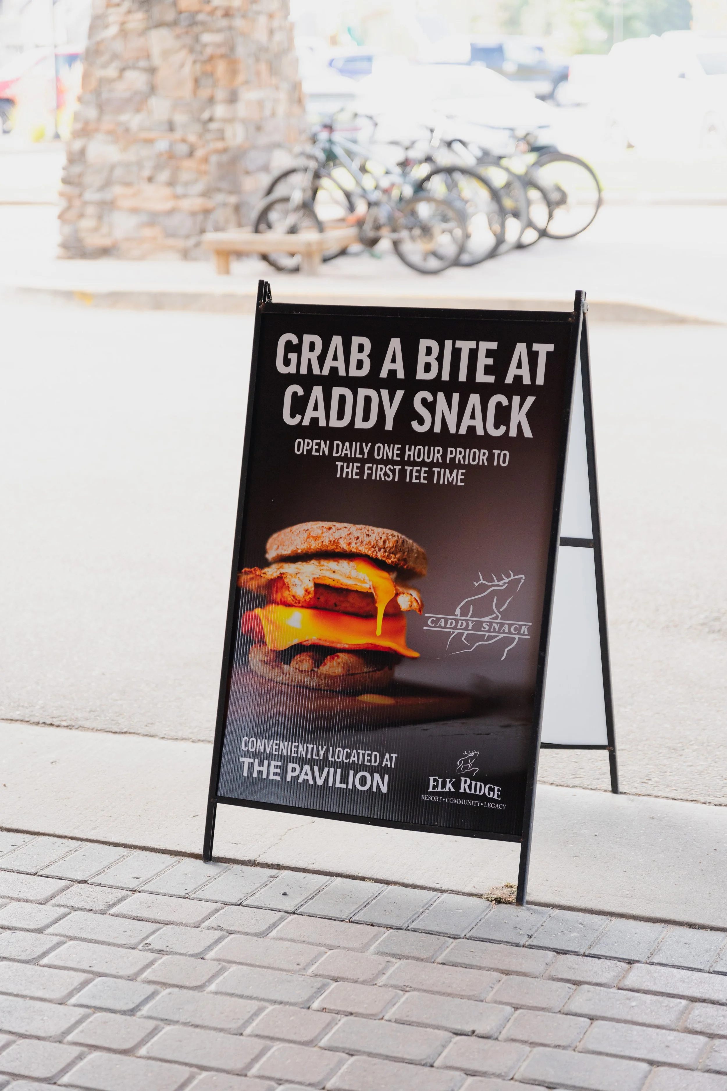 A sidewalk sign for Caddy Snack showing a hamburger and its location at Elk Ridge Resort.