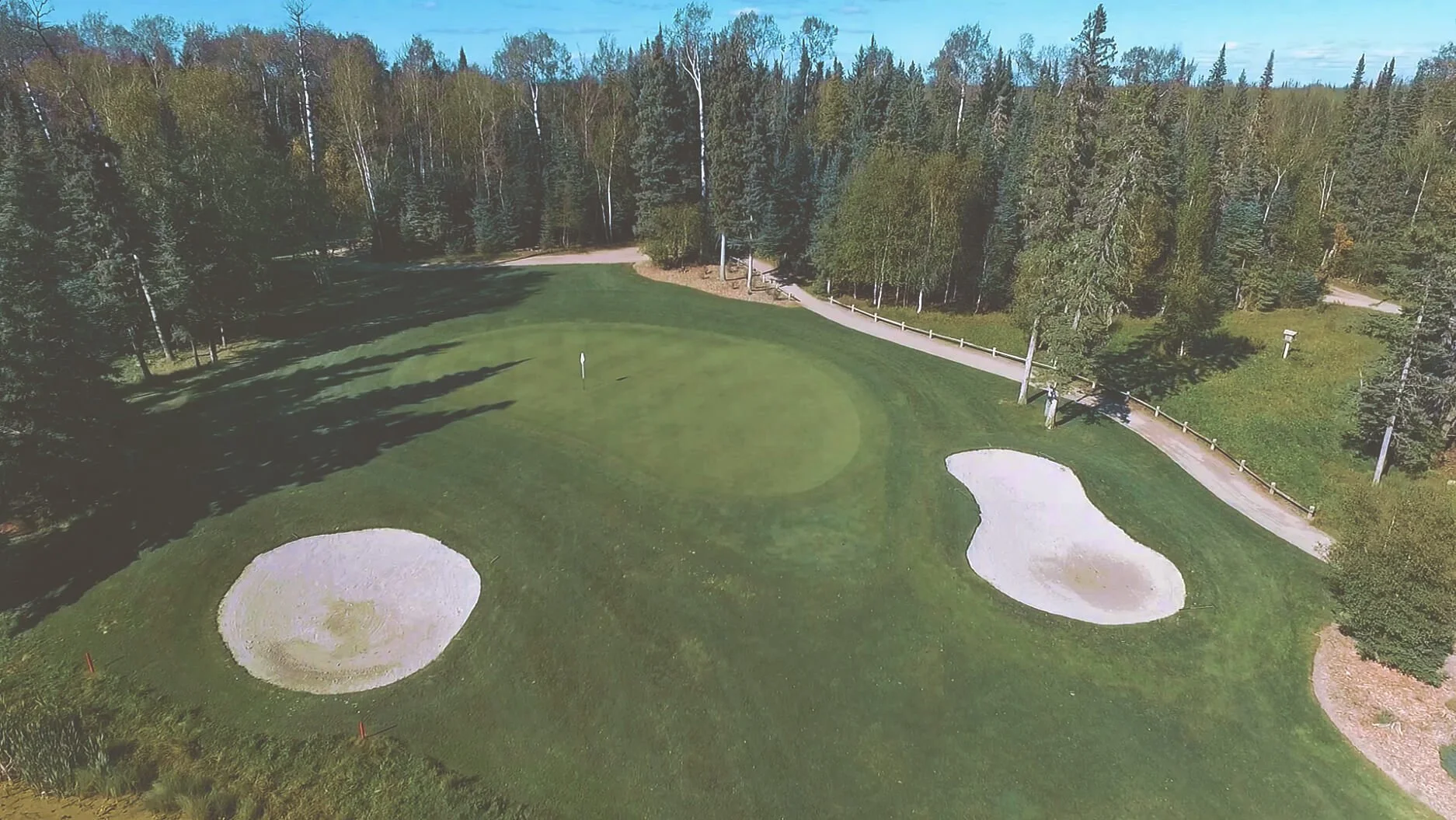 Aerial view of the par 3 second hole on the Tamarack course at Elk Ridge Resort, with water to carry and a bunker beside the green.