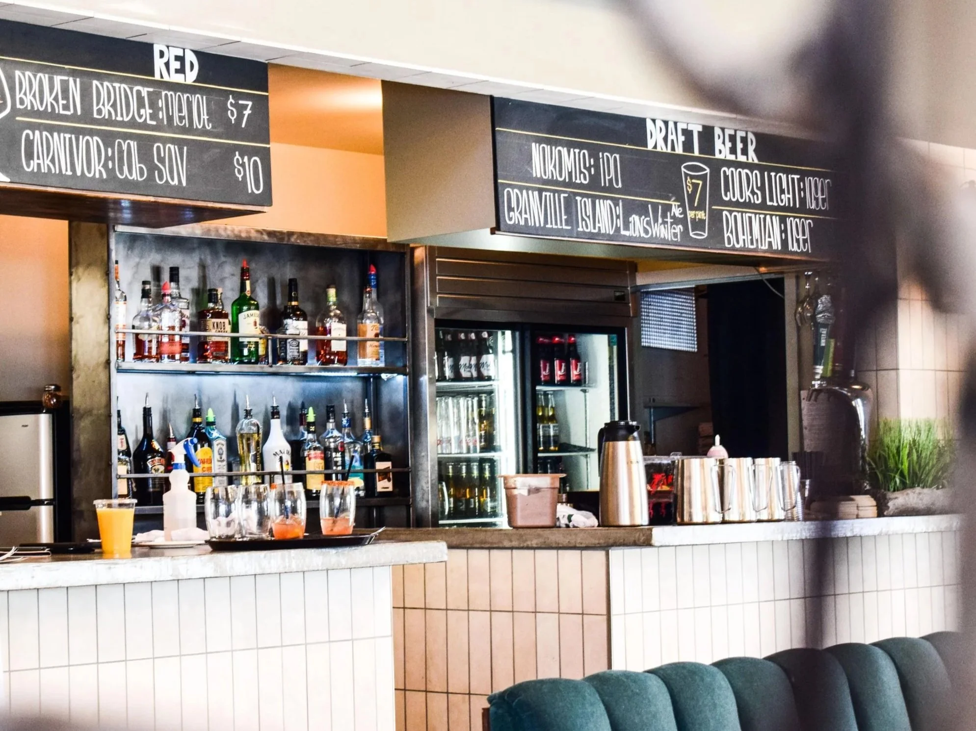 The bar at the Wyld, with bottles on the shelves, a blackboard listing draft beer prices, and drinks on the counter.