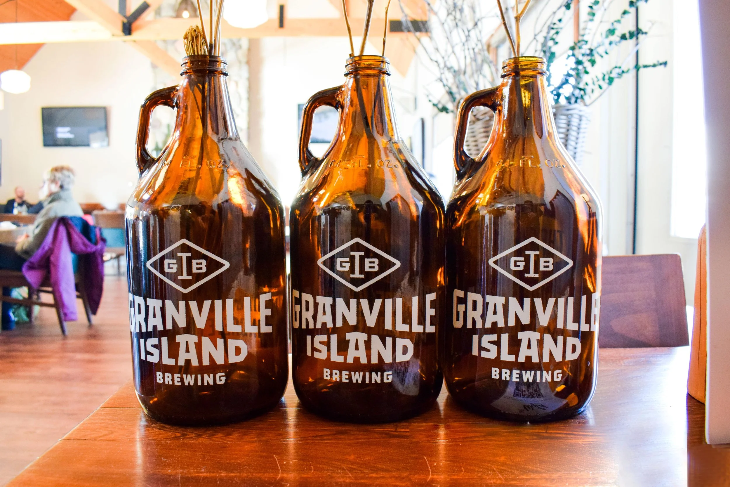 Three amber glass growlers reading &lsquo;Granville Island Brewing&rsquo; on a wooden table in a bright room.