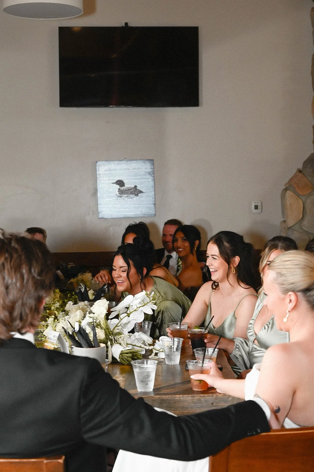 People sitting at a decorated table, smiling and enjoying drinks, with artwork of a loon on the wall behind them.