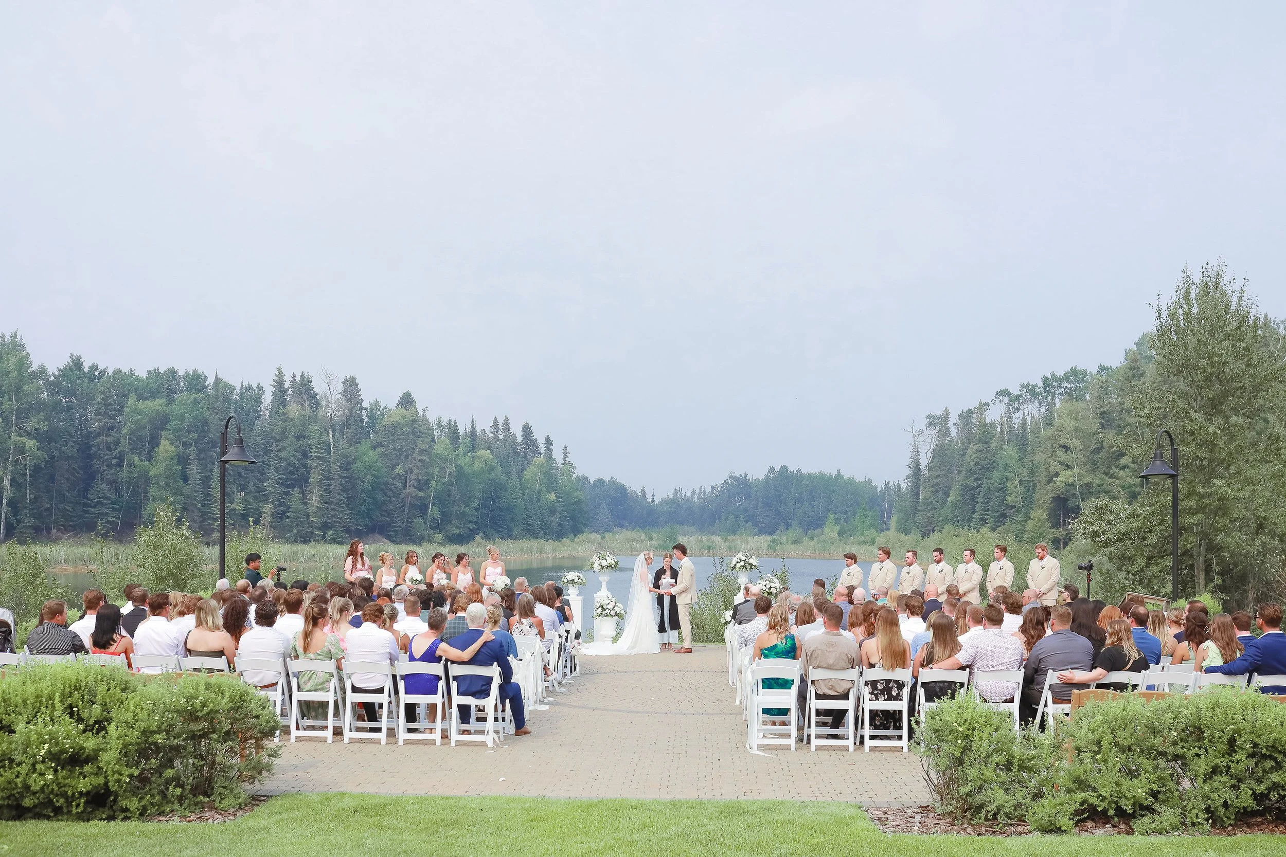 An outdoor wedding ceremony by a river with a backdrop of trees and a cloudy sky.