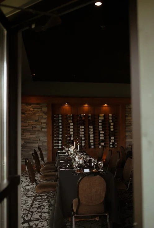 A long dining table set with glasses, plates, and folded napkins, chairs surrounding it.