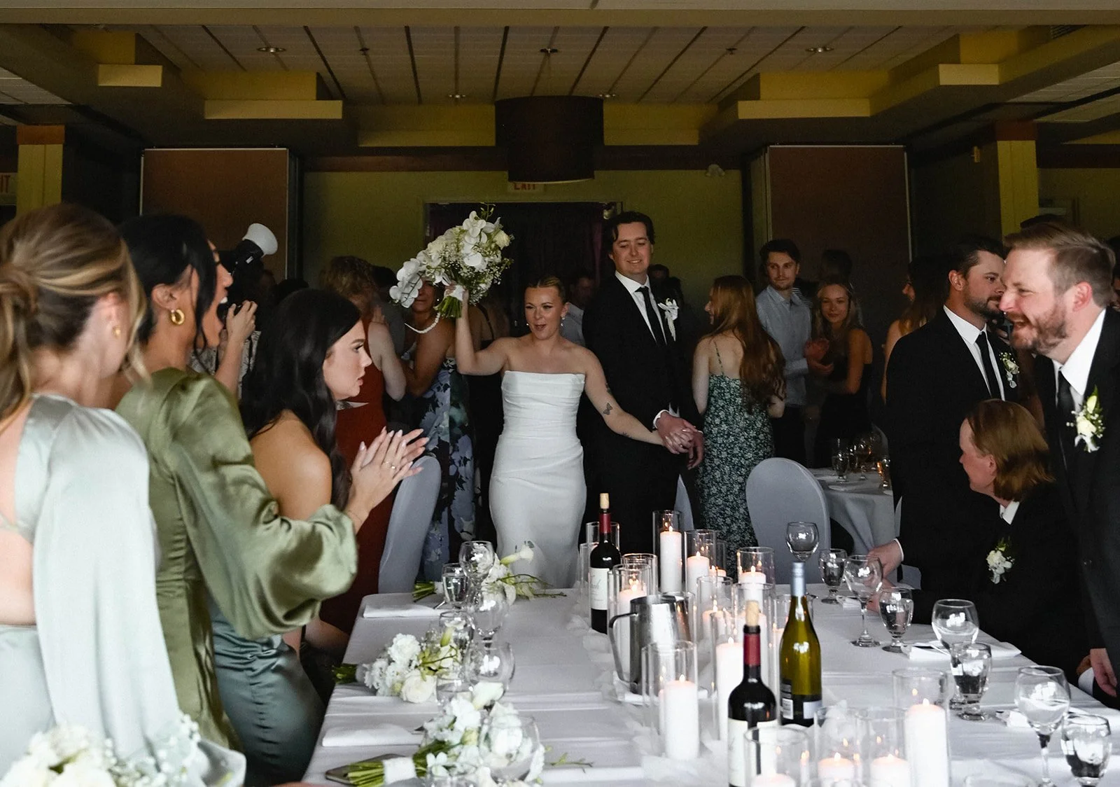 A wedding reception with the bride and groom holding hands and celebrating, surrounded by guests.