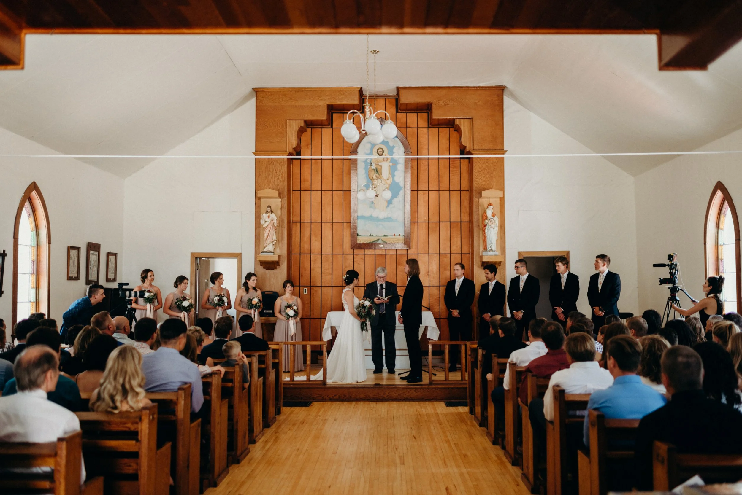 A wedding ceremony inside a church, with the bride and groom standing at the altar before seated guests.