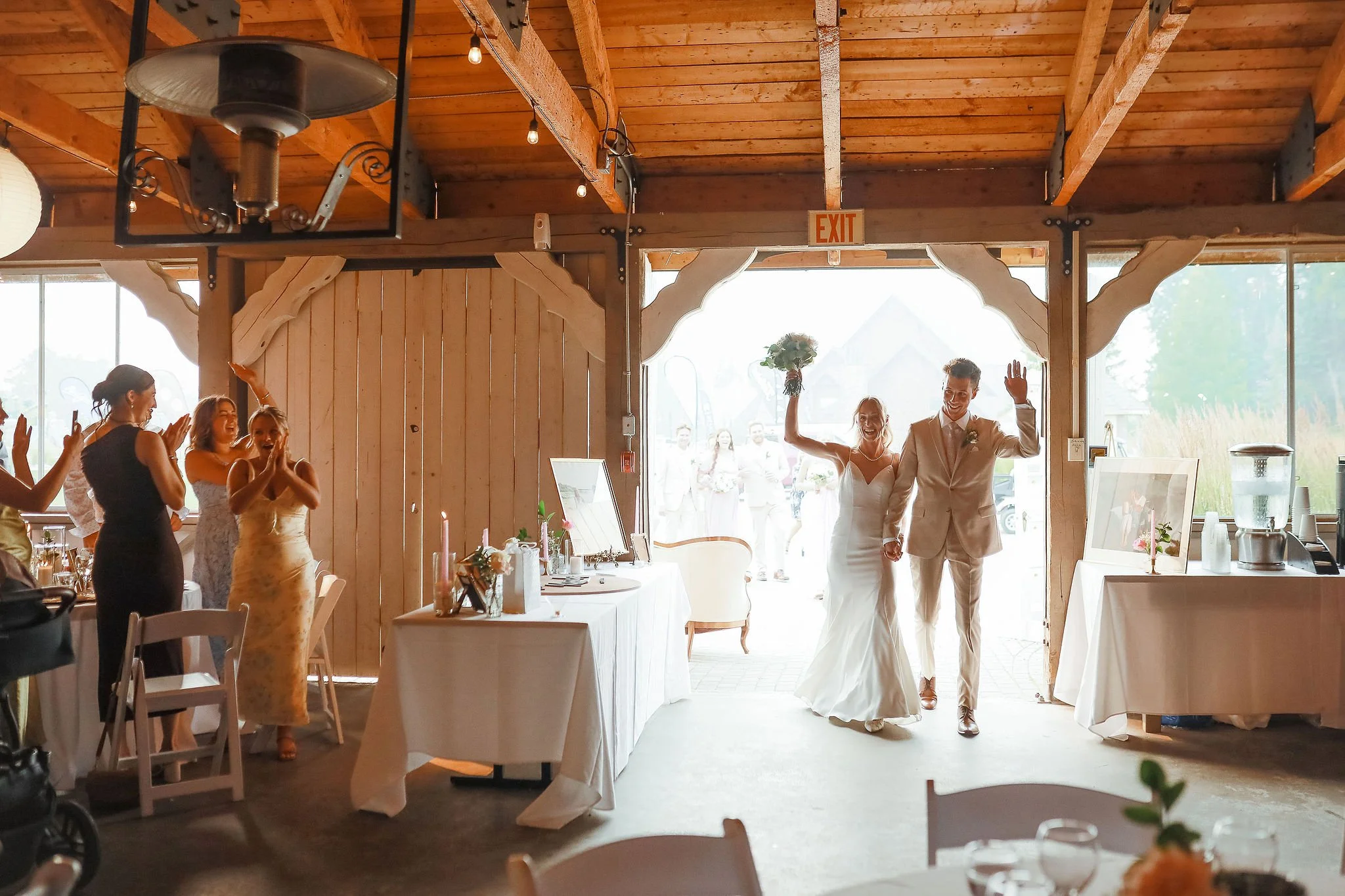 A wedding reception scene with a bride and groom smiling and waving as they enter the room.