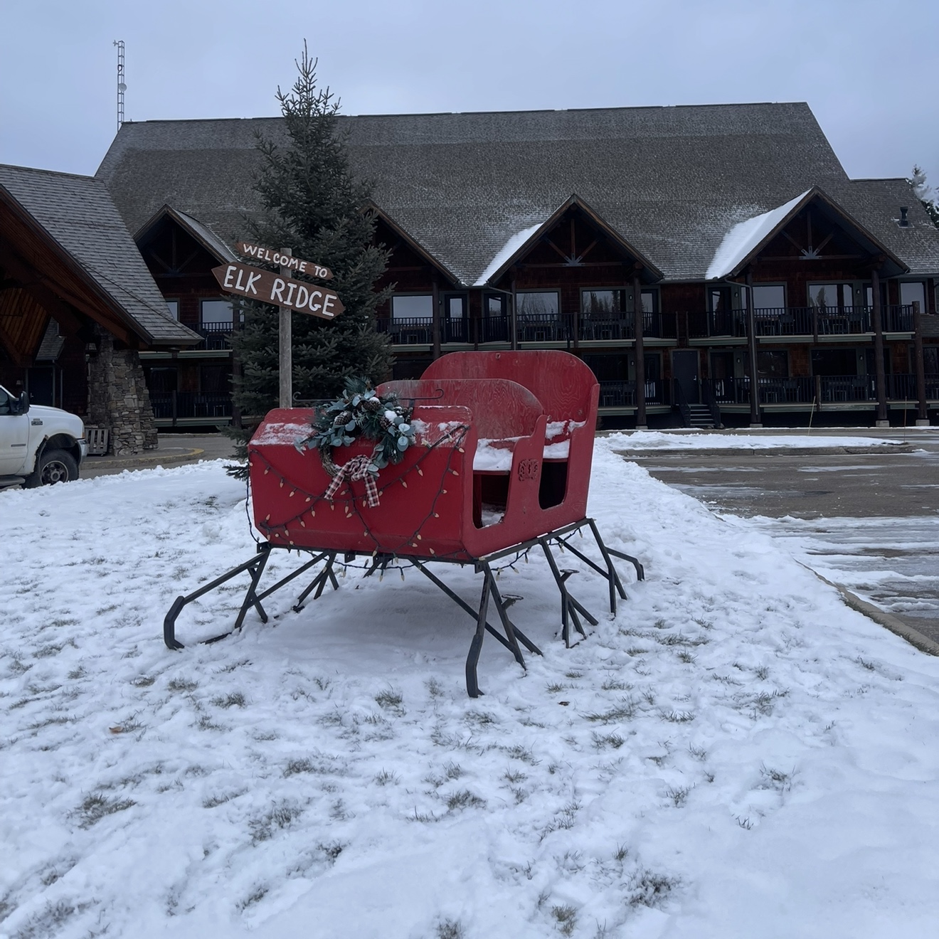 A red sleigh trimmed with a wreath and lights on the snow in front of the Lodge at Elk Ridge Resort