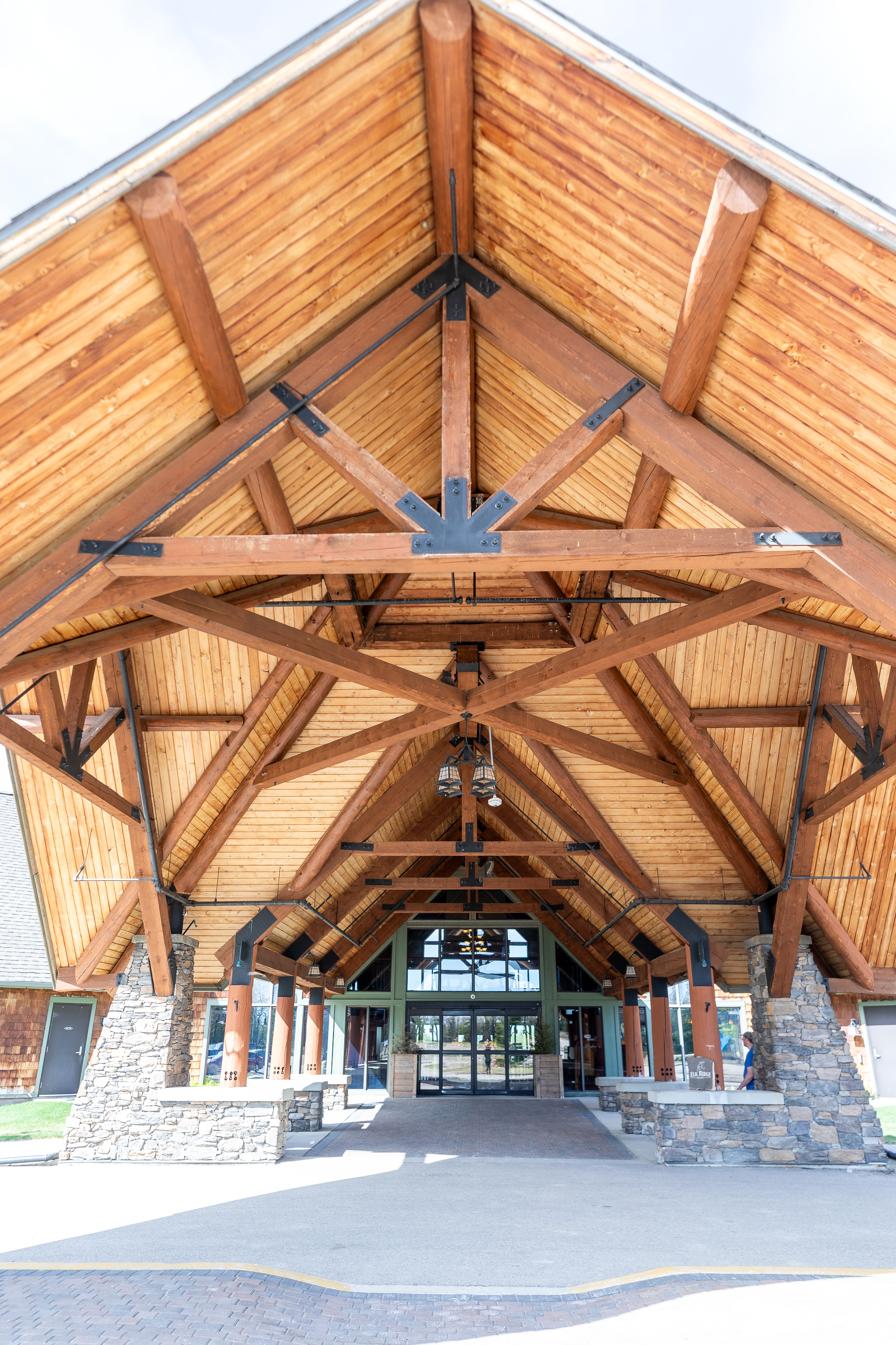 Timber trusses of the Lodge entrance canopy seen from below, framing the glass front doors