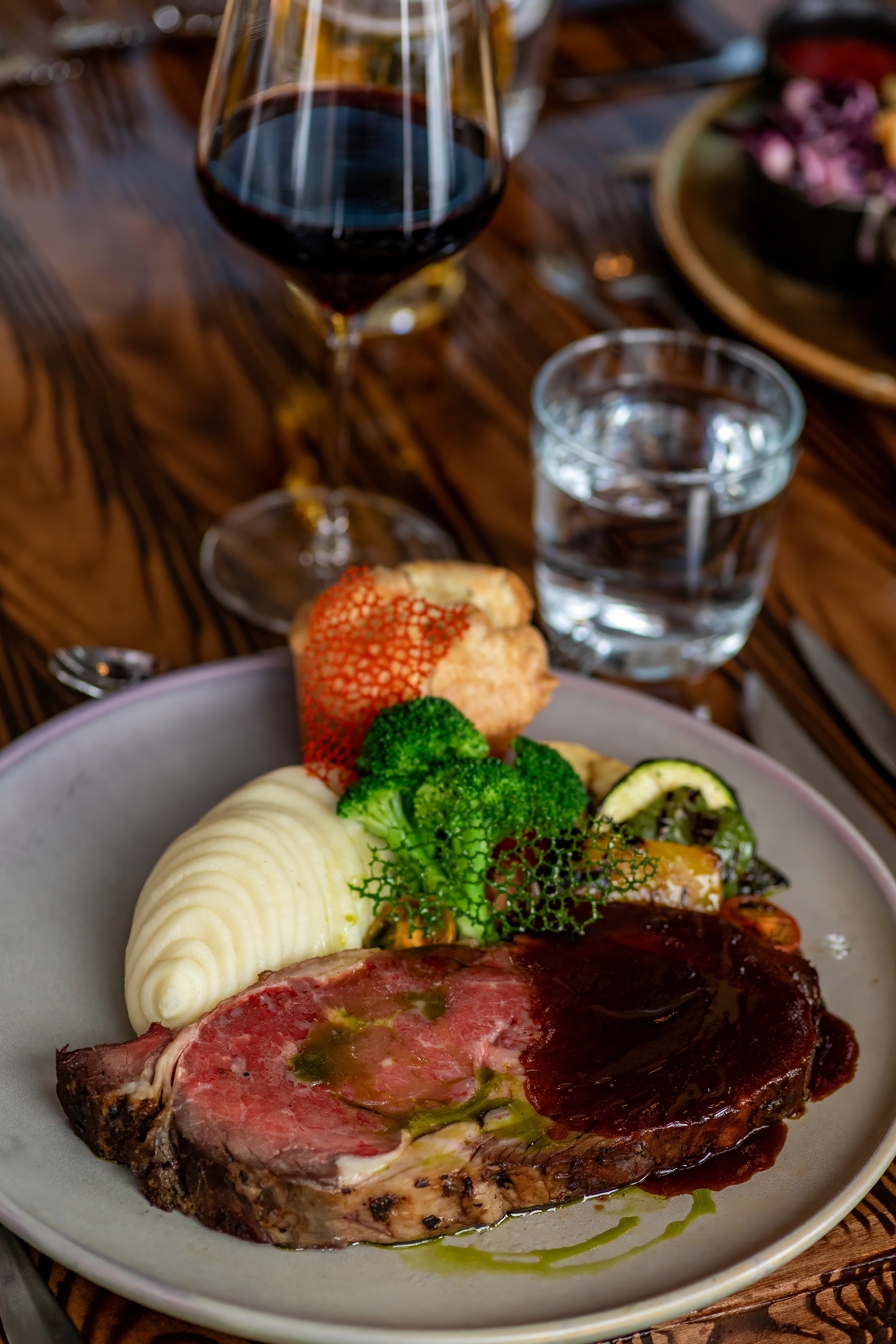 Prime rib with mashed potatoes, broccoli and Yorkshire pudding beside a glass of red wine