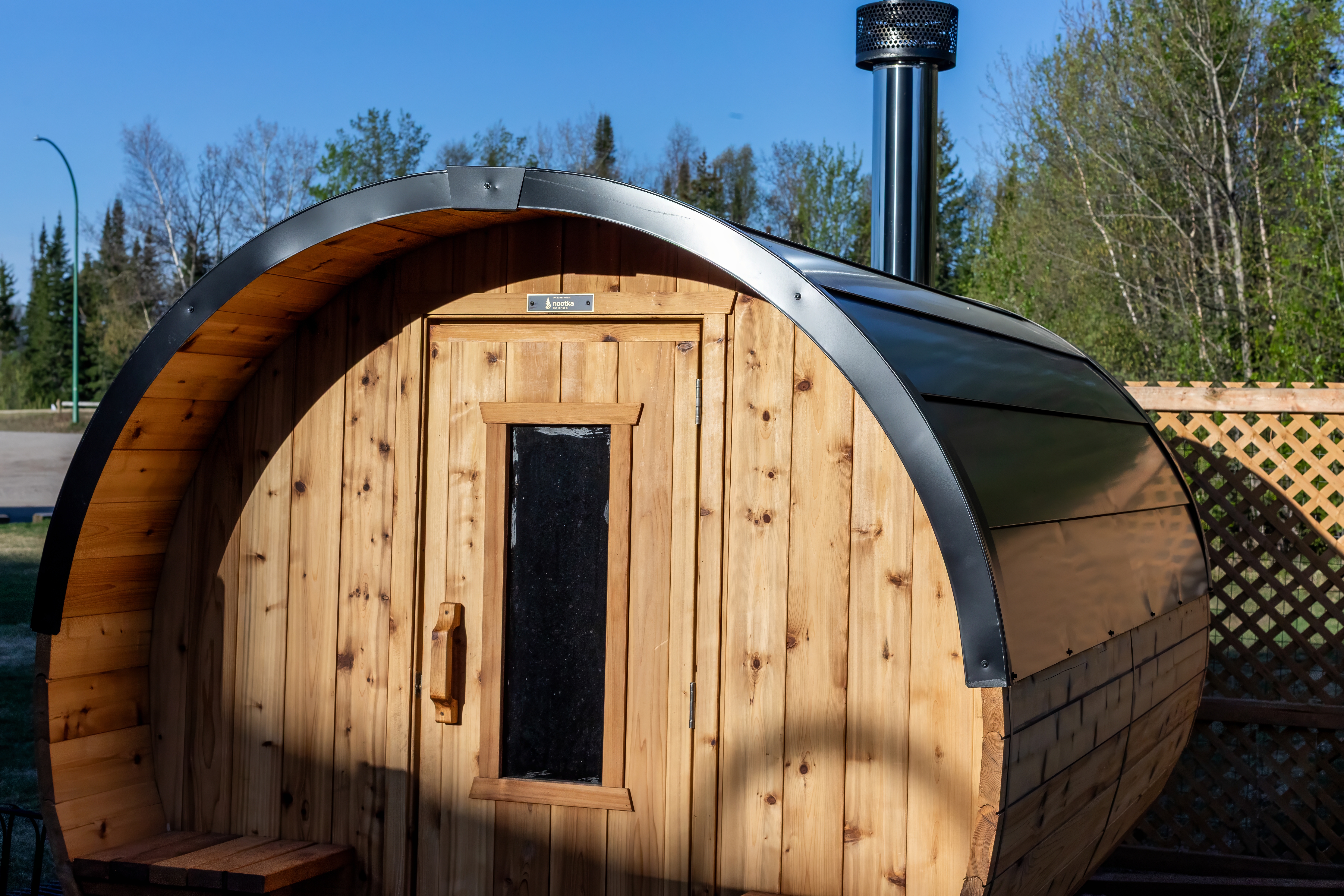 Cedar barrel sauna with its stove chimney and forest behind
