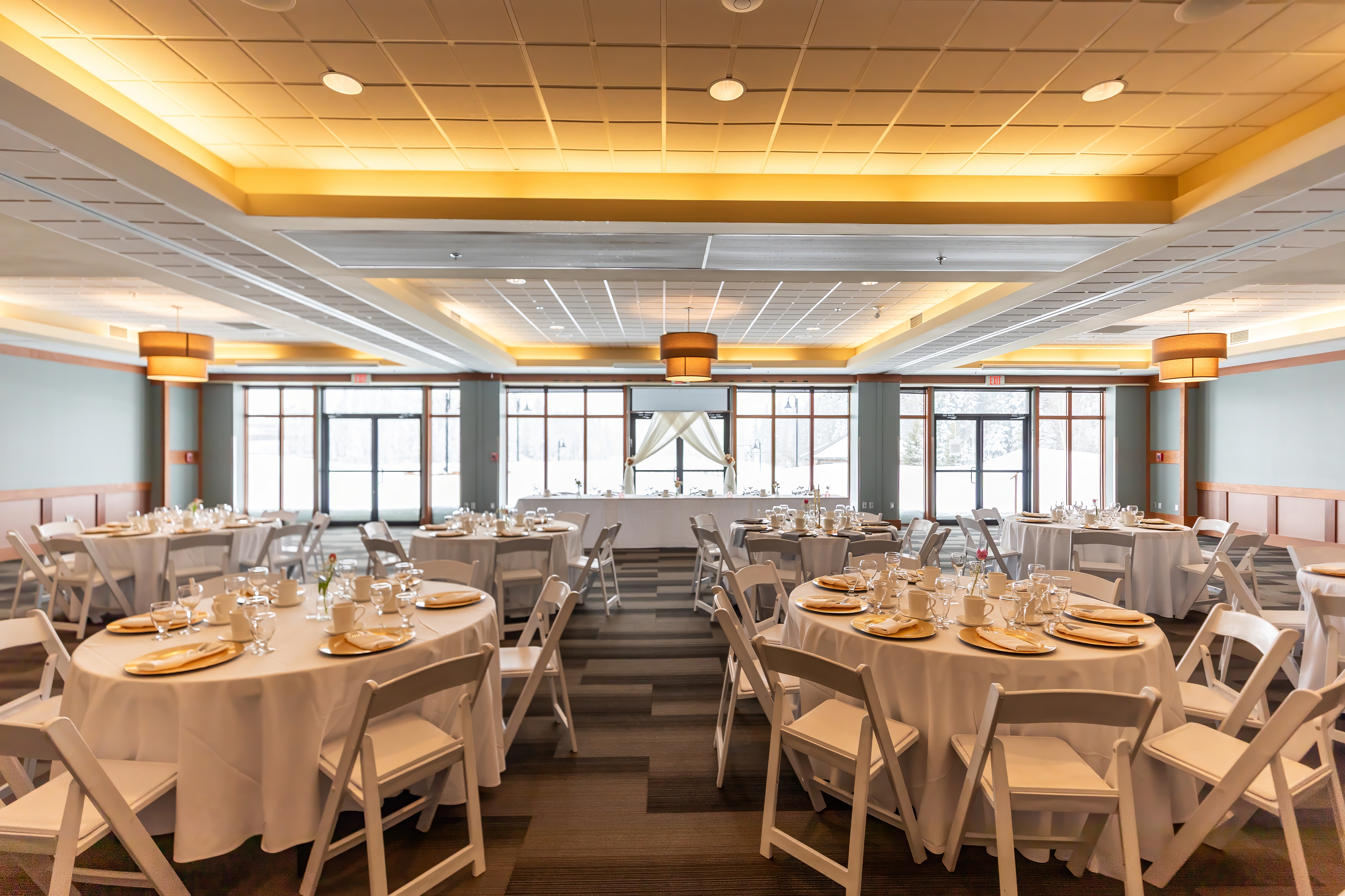 Ballroom set for a wedding reception with round tables, gold chargers and white folding chairs