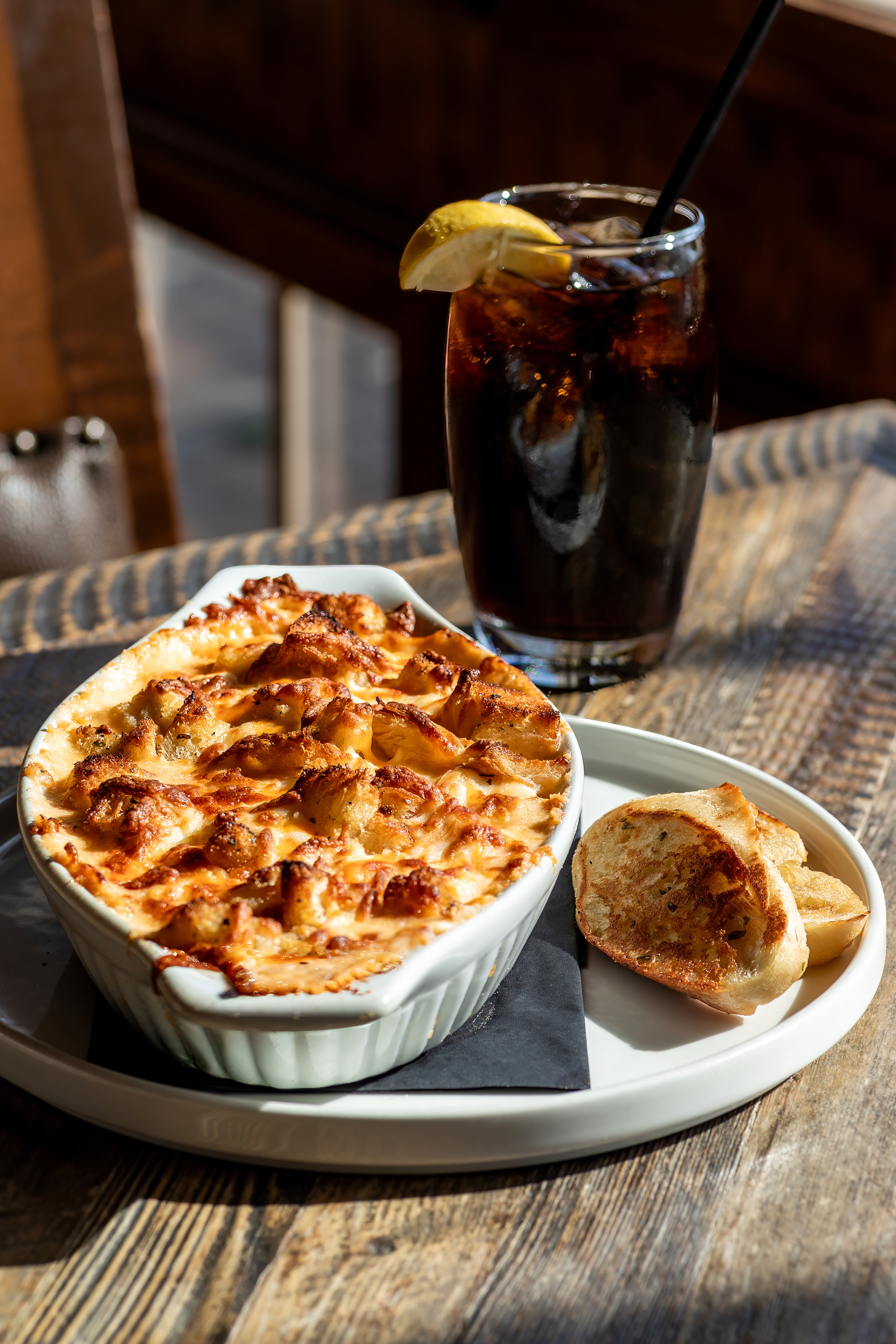 Baked mac and cheese with garlic toast and an iced cola on a sunlit wooden table at the Wyld